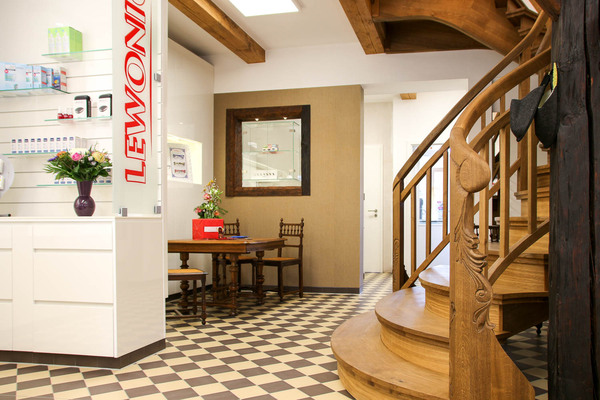 Heller Eingangsbereich eines Optikers mit Holztreppe, Beratungstisch und Brillenausstellung.