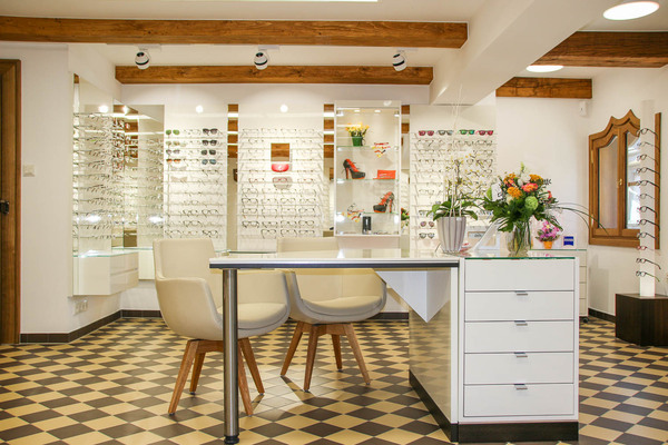 Modernes Optiker-Fachgeschäft mit Brillenauswahl, Beratungstisch und Blumenarrangement.